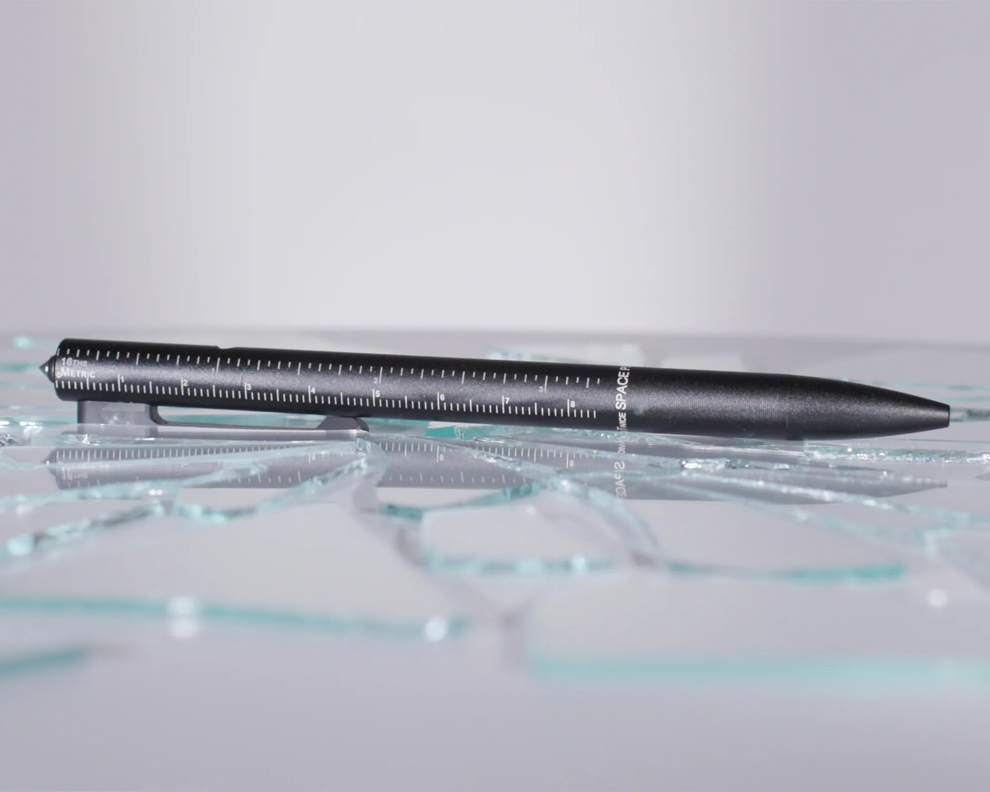 Black pen with white metric ruler markings lying on shattered glass pieces.