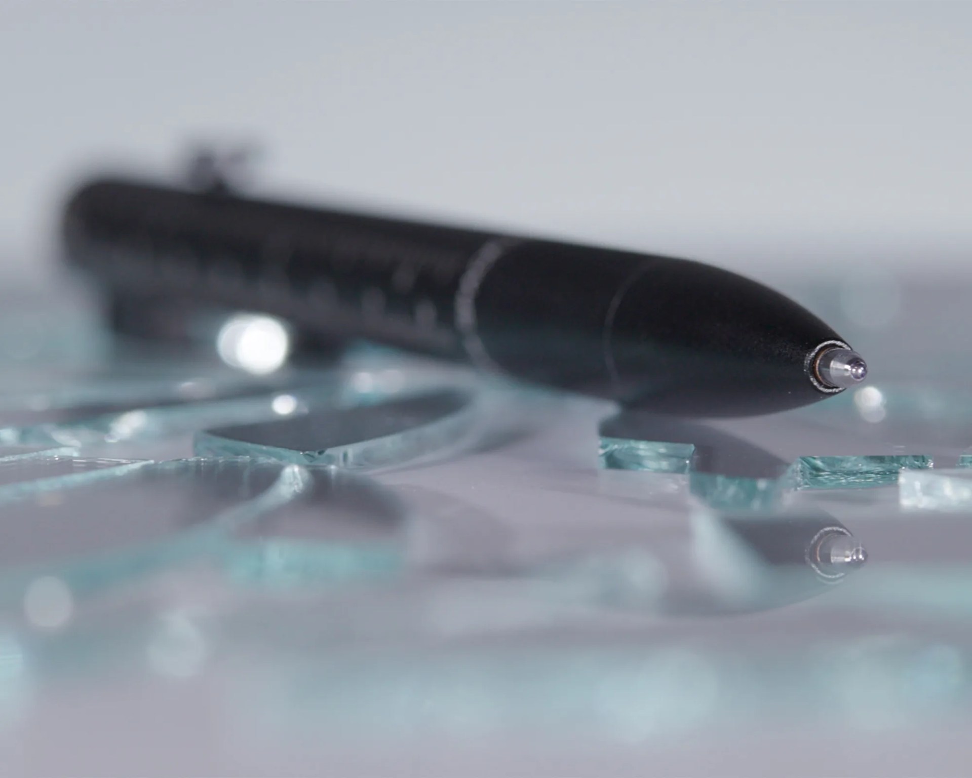 Black ballpoint pen lying on scattered broken glass pieces on a reflective surface.