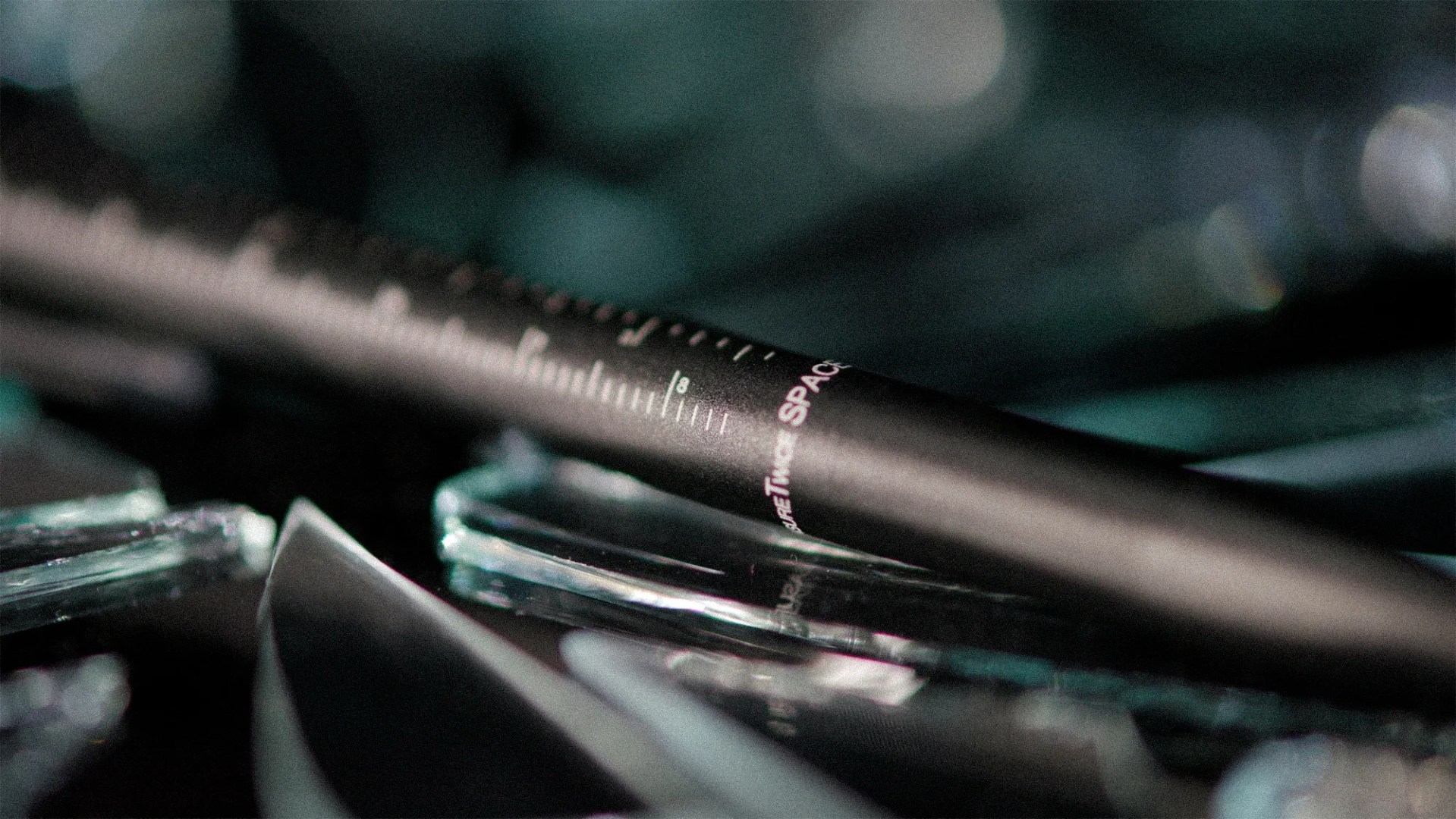 Close-up of a black pen with white measurement markings and the word "SPACE" in pink on a reflective surface.
