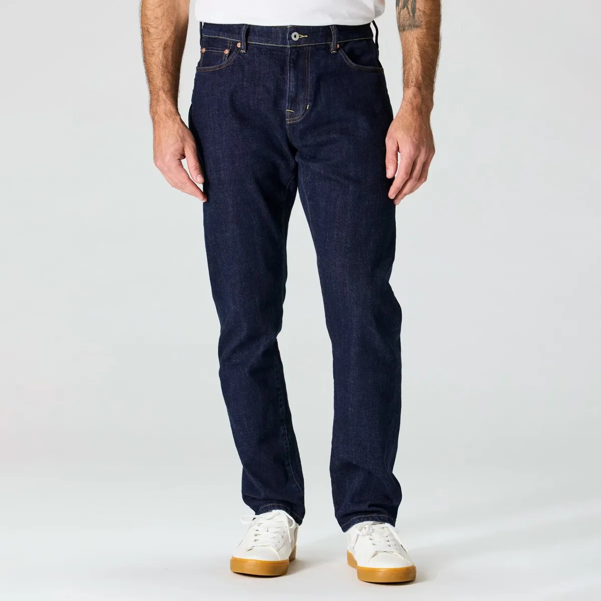 Dark indigo straight-leg jeans worn with white sneakers on a plain background.