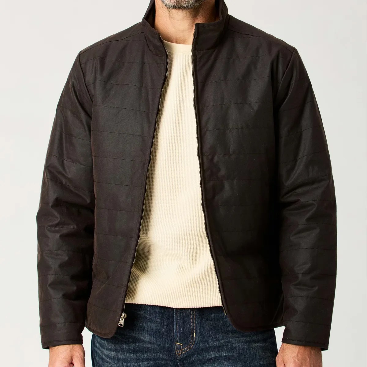 Black quilted zip-up jacket worn over a cream ribbed sweater and blue jeans.