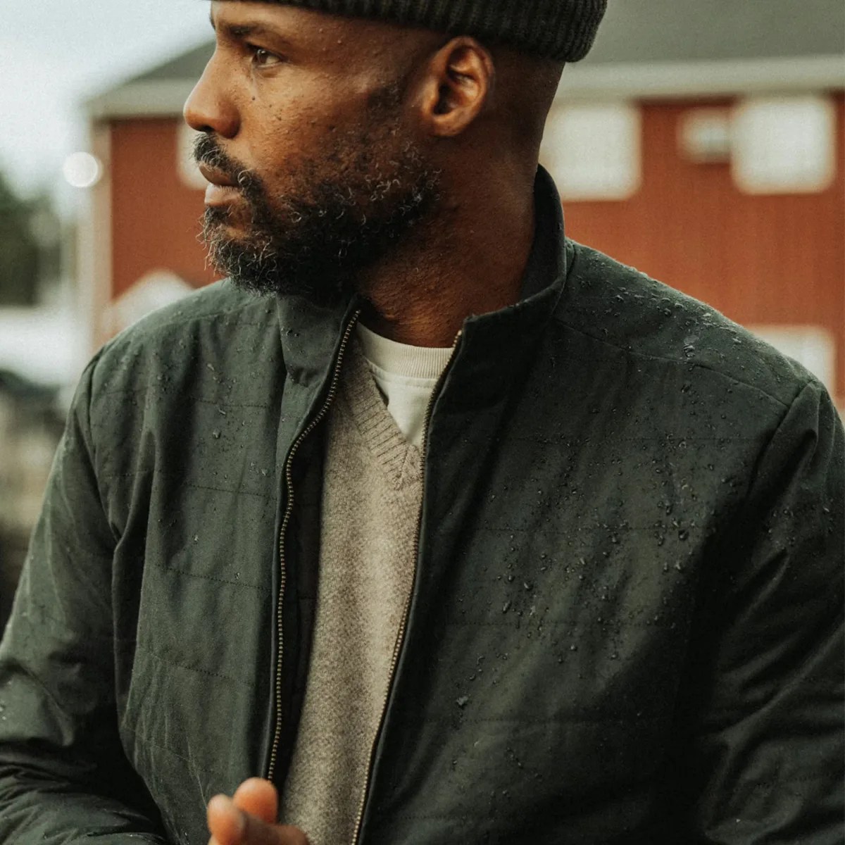 Man wearing a dark green water-resistant jacket with visible water droplets and a knit beanie.