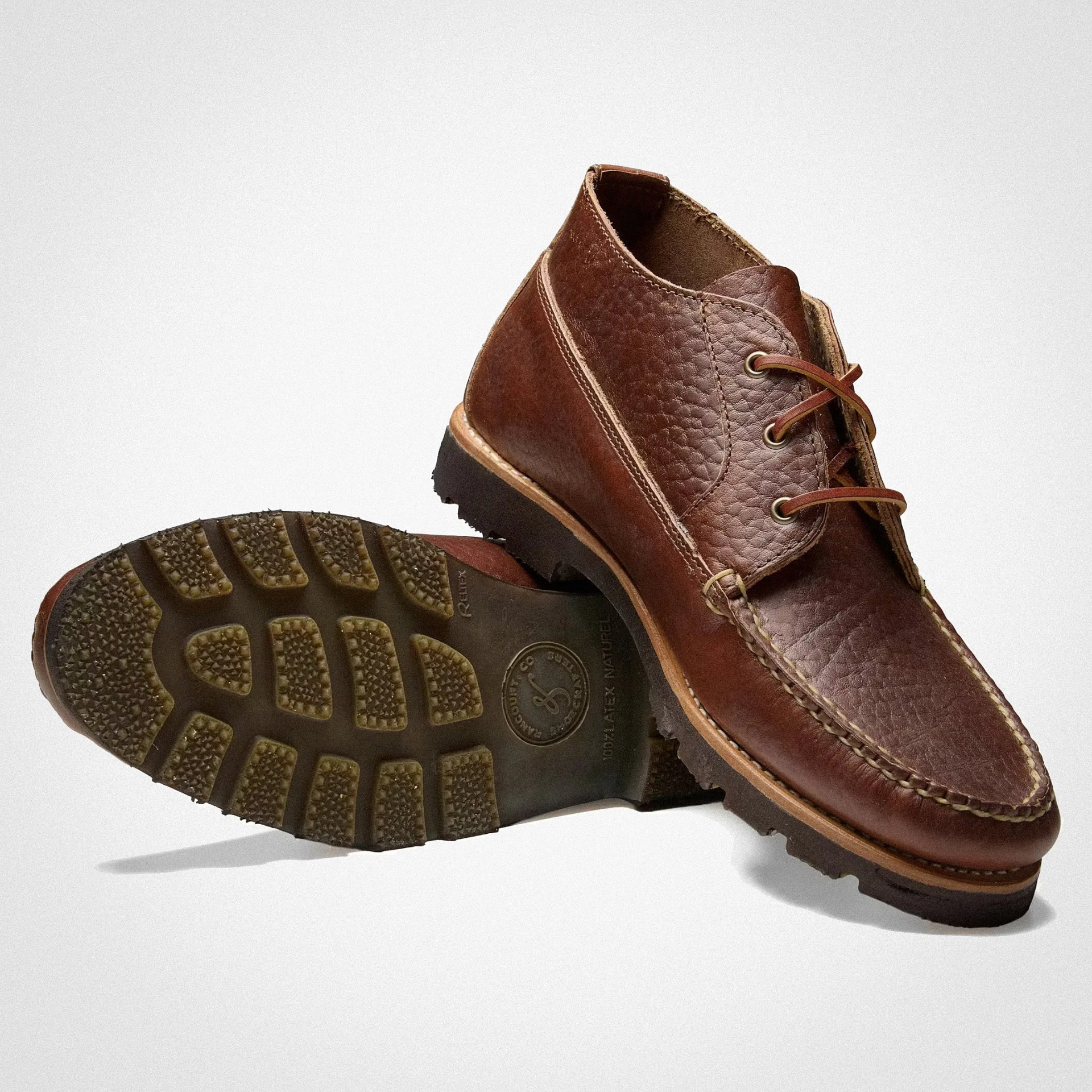 Pair of brown leather moccasin-style boots with textured uppers and rugged rubber soles, one showing the sole tread.