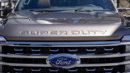 Close-up of a gray Ford truck hood with "SUPER DUTY" embossed and a chrome grille with Ford emblem.