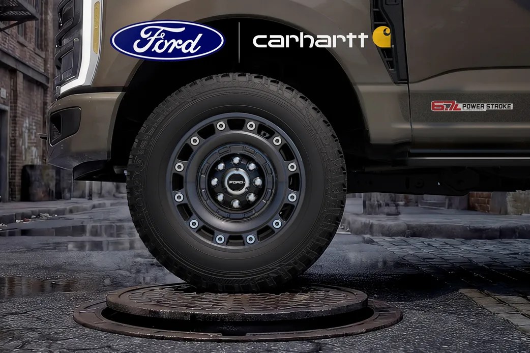 Close-up of a black Ford truck tire on a wet cobblestone street with Ford and Carhartt logos above.
