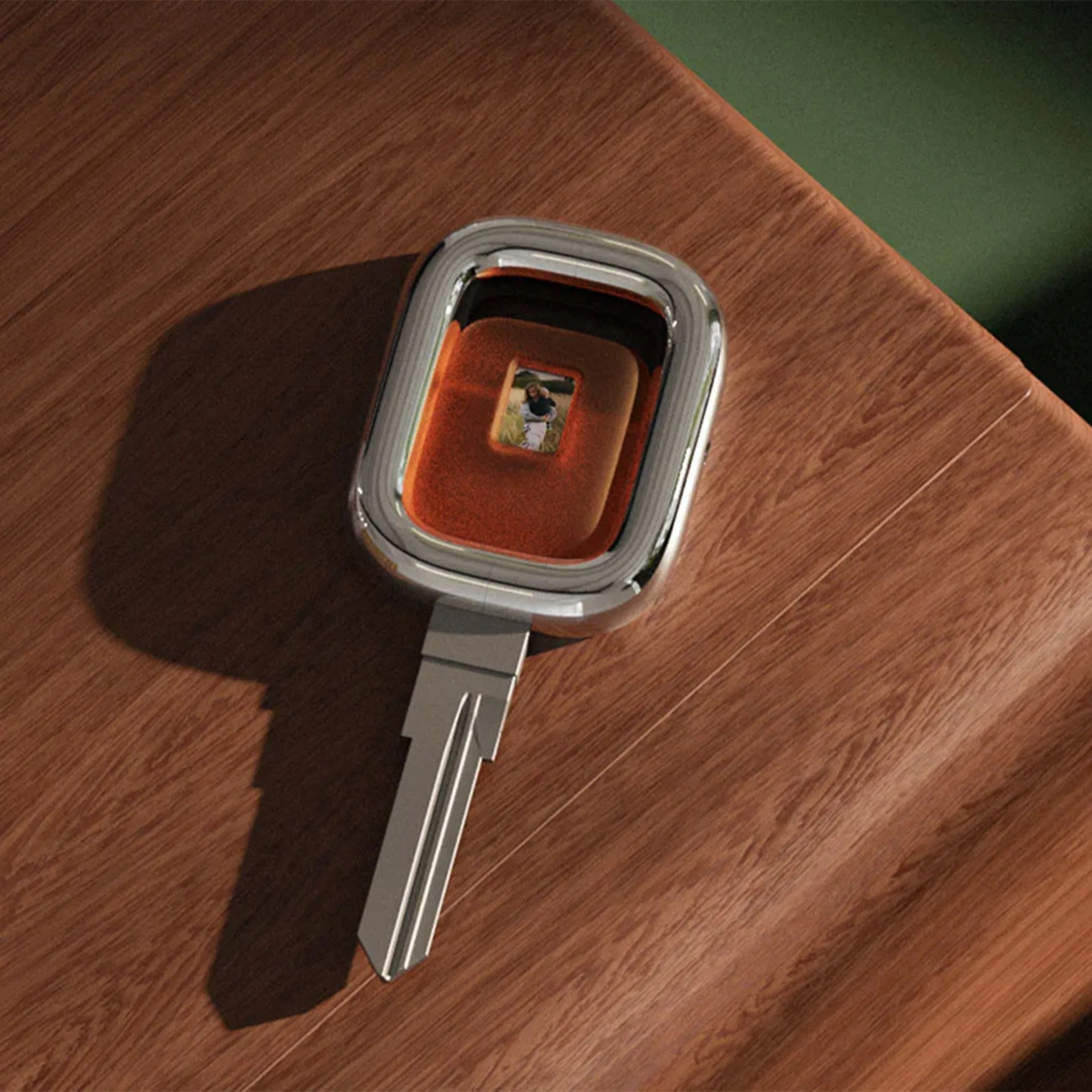 Silver and orange smart key with a small digital screen displaying a photo, placed on a wooden surface.