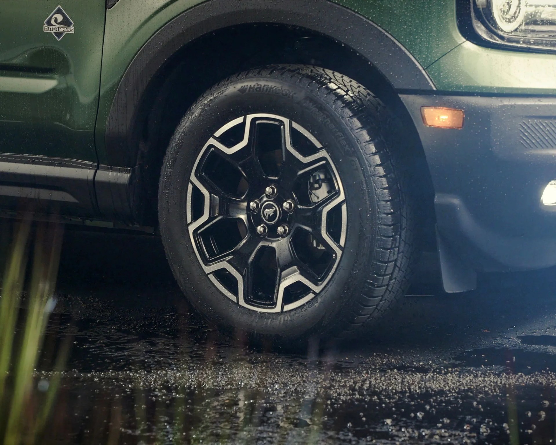 Black and silver alloy wheel with Hankook tire on a green vehicle with Outer Banks badge.