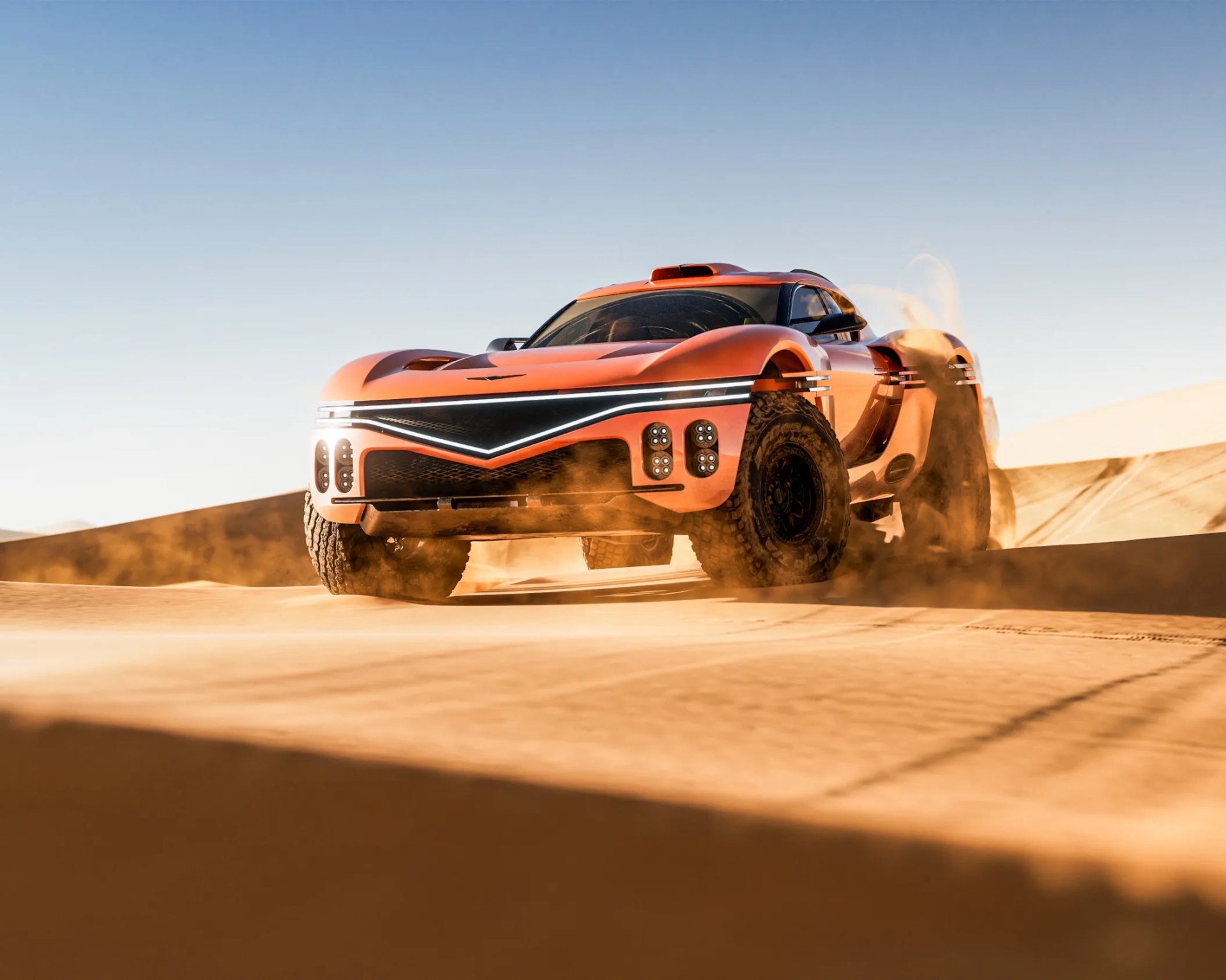 Orange off-road vehicle kicking up sand while driving on desert dunes under a clear sky.
