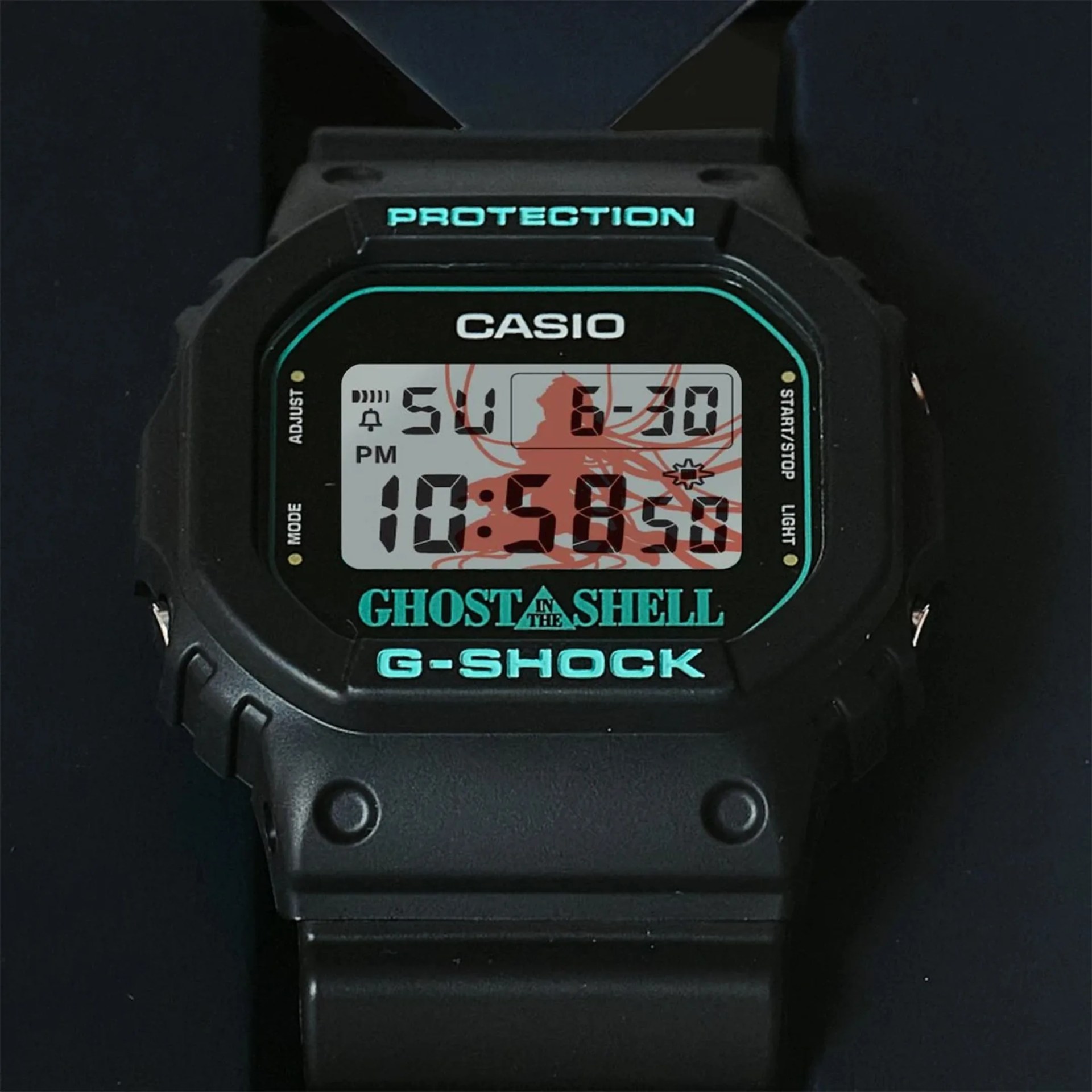 Black Casio G-Shock digital watch with turquoise "Ghost in the Shell" branding and red graphic on display.