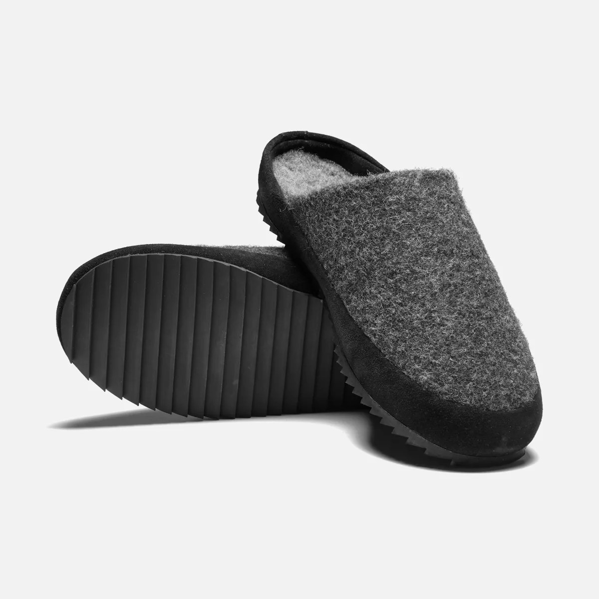 Pair of gray felt slip-on slippers with black rubber soles, one showing the textured bottom.