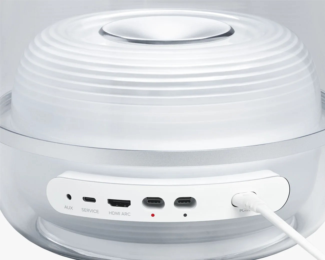 White circular electronic device with AUX, service, HDMI ARC, two USB-C ports, and power cable connected.