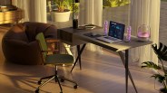 Modern home office setup with a laptop, purple-lit speakers, and a glass humidifier on a sleek desk with a green swivel chair and brown bean bag.