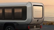 Rear side view of a silver Honda electric camper van with tinted windows parked near a beach at sunset.