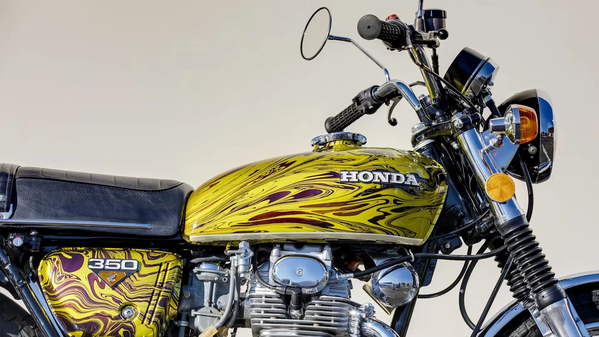 Yellow and maroon swirled Honda 350 motorcycle fuel tank and side cover with black seat and chrome engine parts.