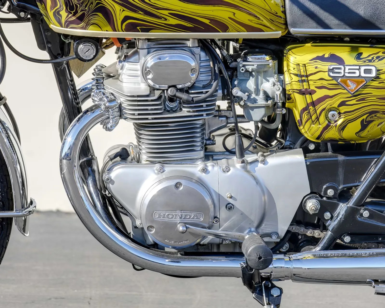 Close-up of a silver Honda motorcycle engine with a yellow and black marbled fuel tank and side cover labeled "350.