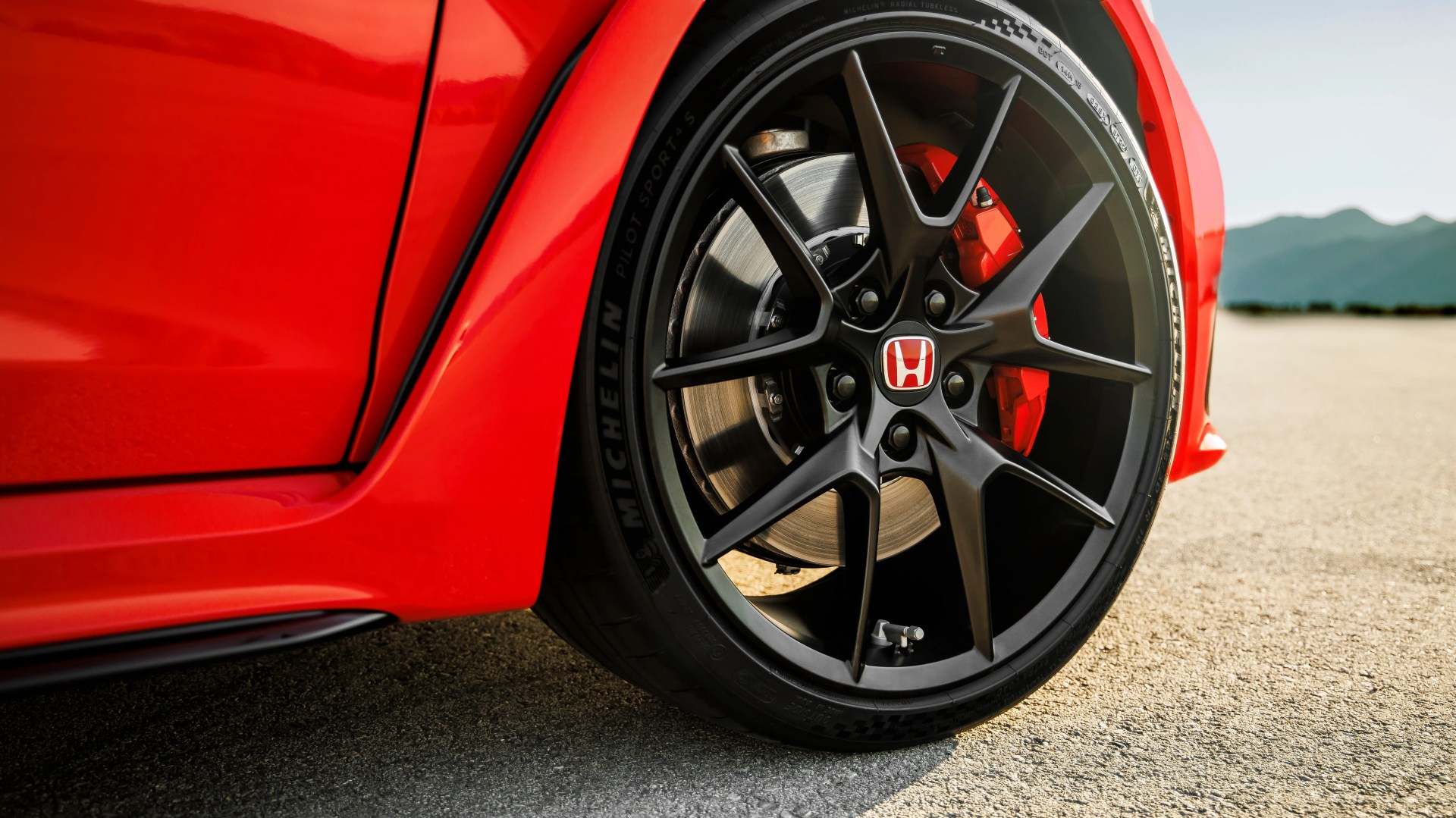 Close-up of a black Honda alloy wheel with red brake caliper on a red car parked on asphalt.