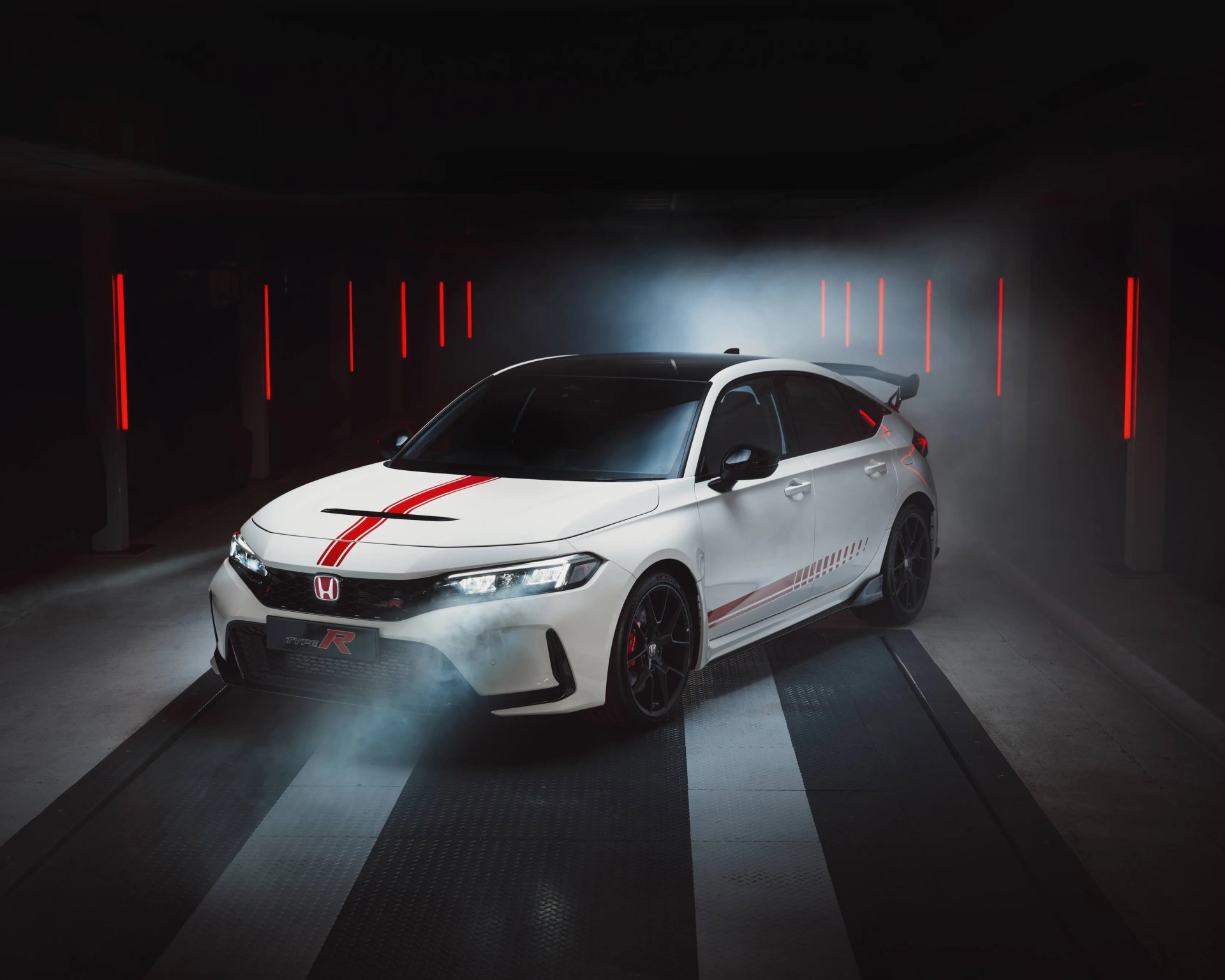 White Honda Type R hatchback with red racing stripes and black wheels in a dimly lit garage with red vertical lights.