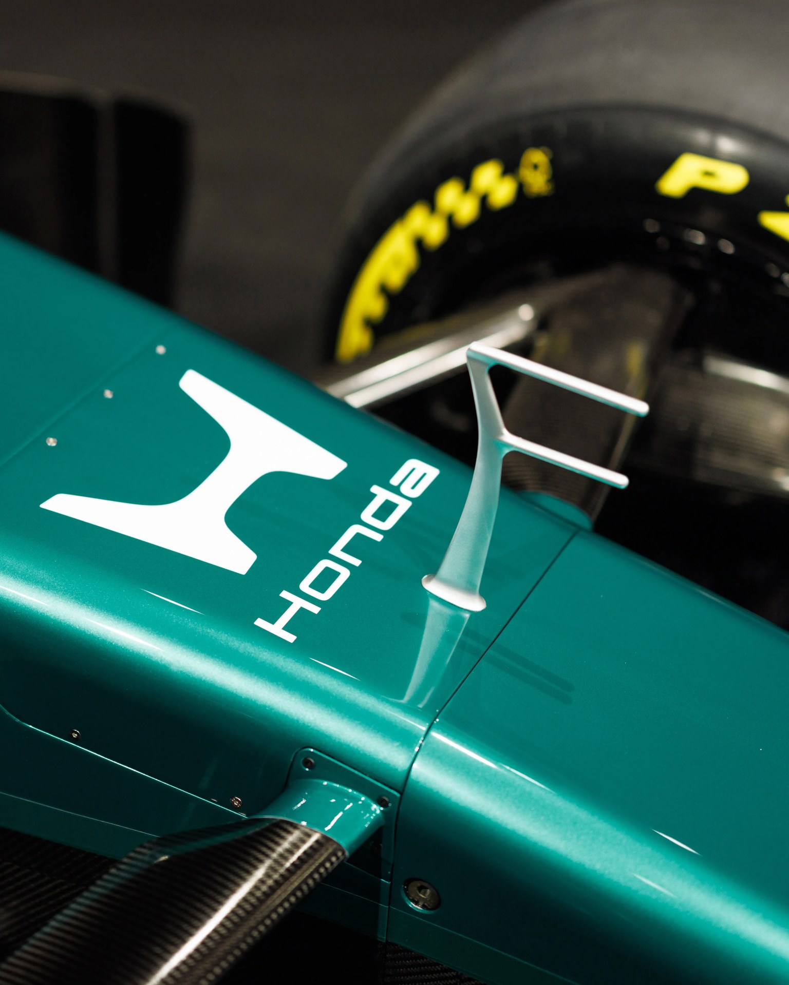 Close-up of a teal Honda Formula 1 car body with a silver aerodynamic fin and a Pirelli tire in the background.
