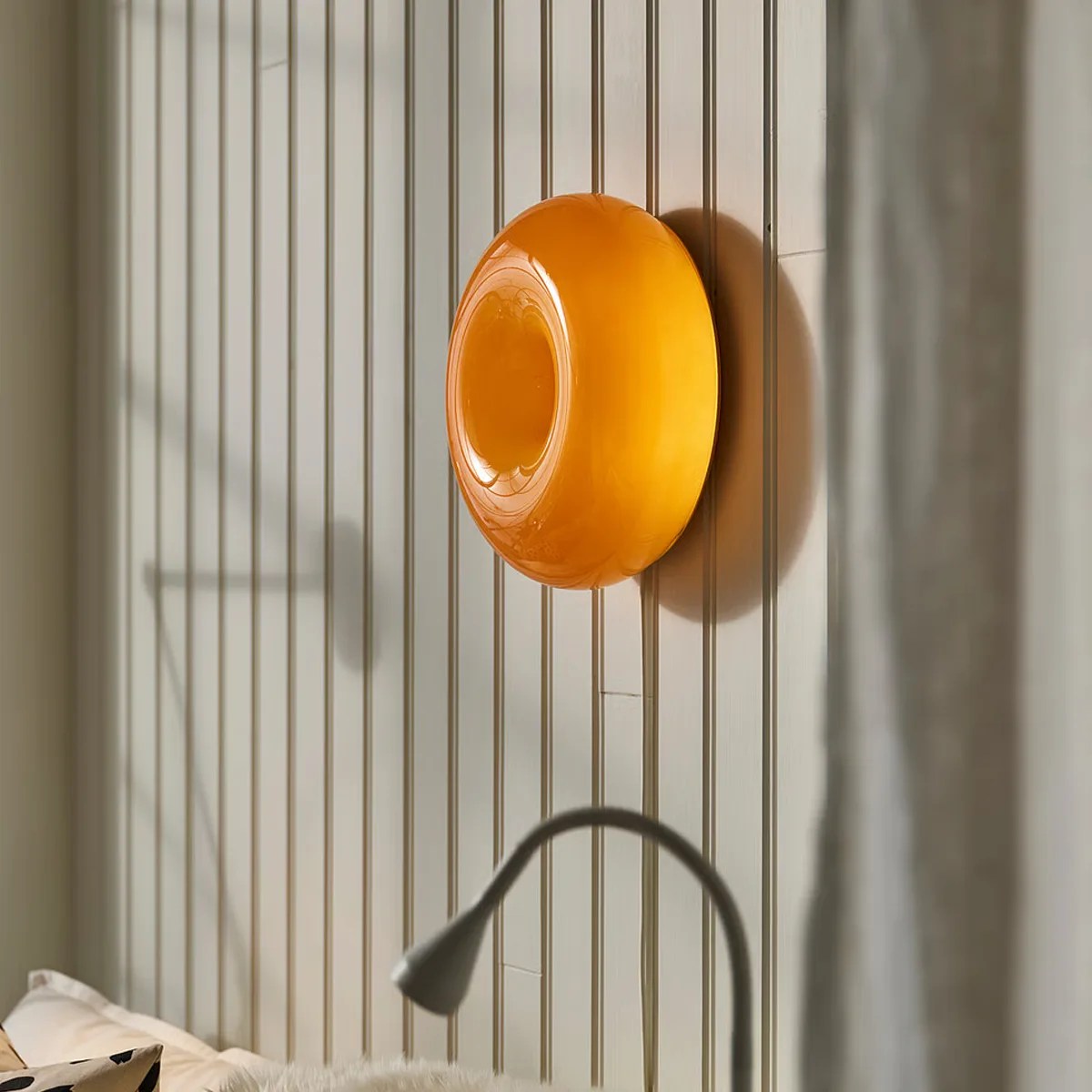 Round amber-colored wall lamp mounted on a vertically paneled beige wall.