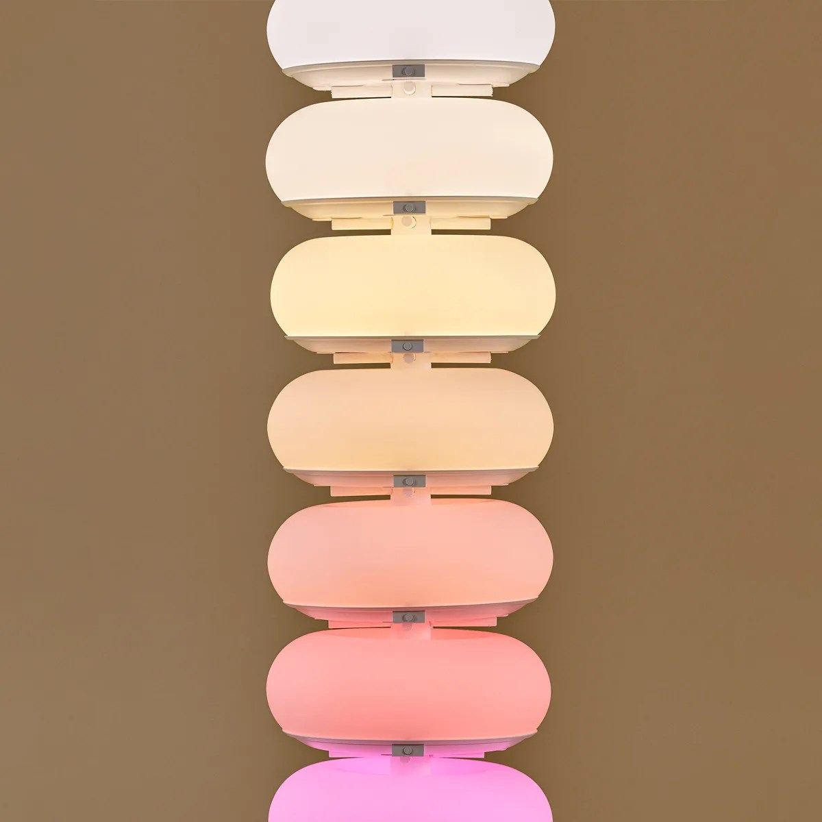 Seven oval-shaped wall lights in a vertical row showing a gradient from white to pink light on a brown wall.