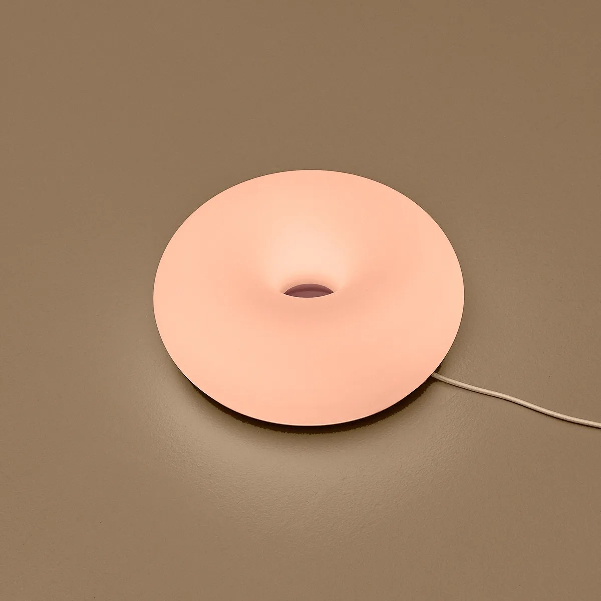 Round peach-colored donut-shaped lamp with a central hole on a brown surface.