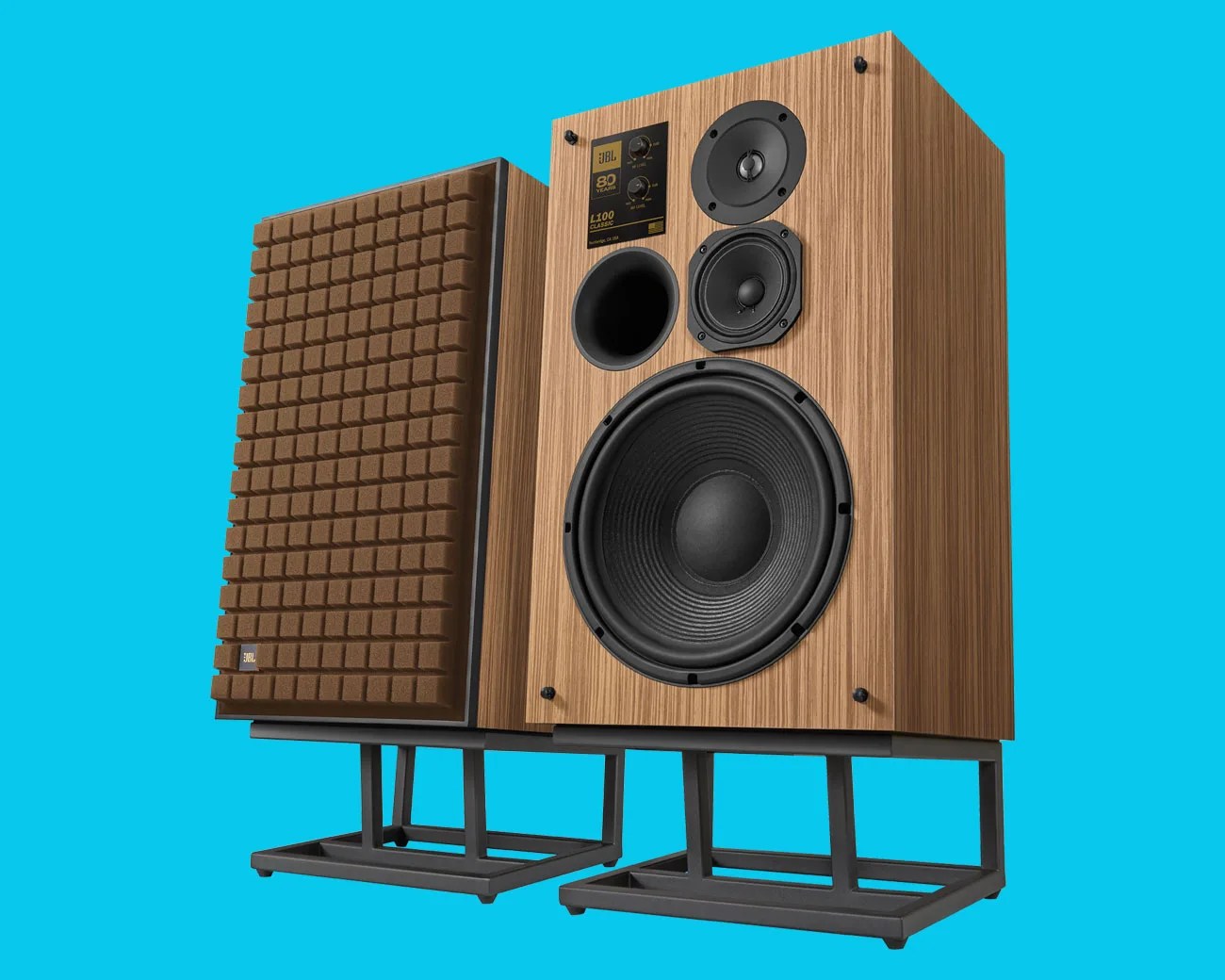 Pair of vintage JBL L100 Classic speakers with wood veneer finish and brown foam grills on black metal stands.