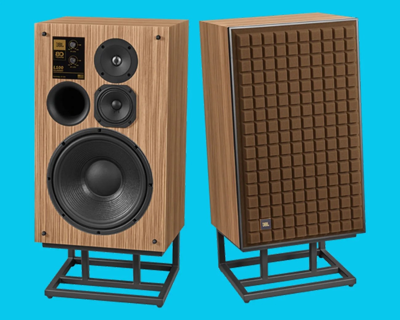 Pair of vintage JBL L100 Classic speakers with wood veneer finish and brown foam grille covers on black metal stands.