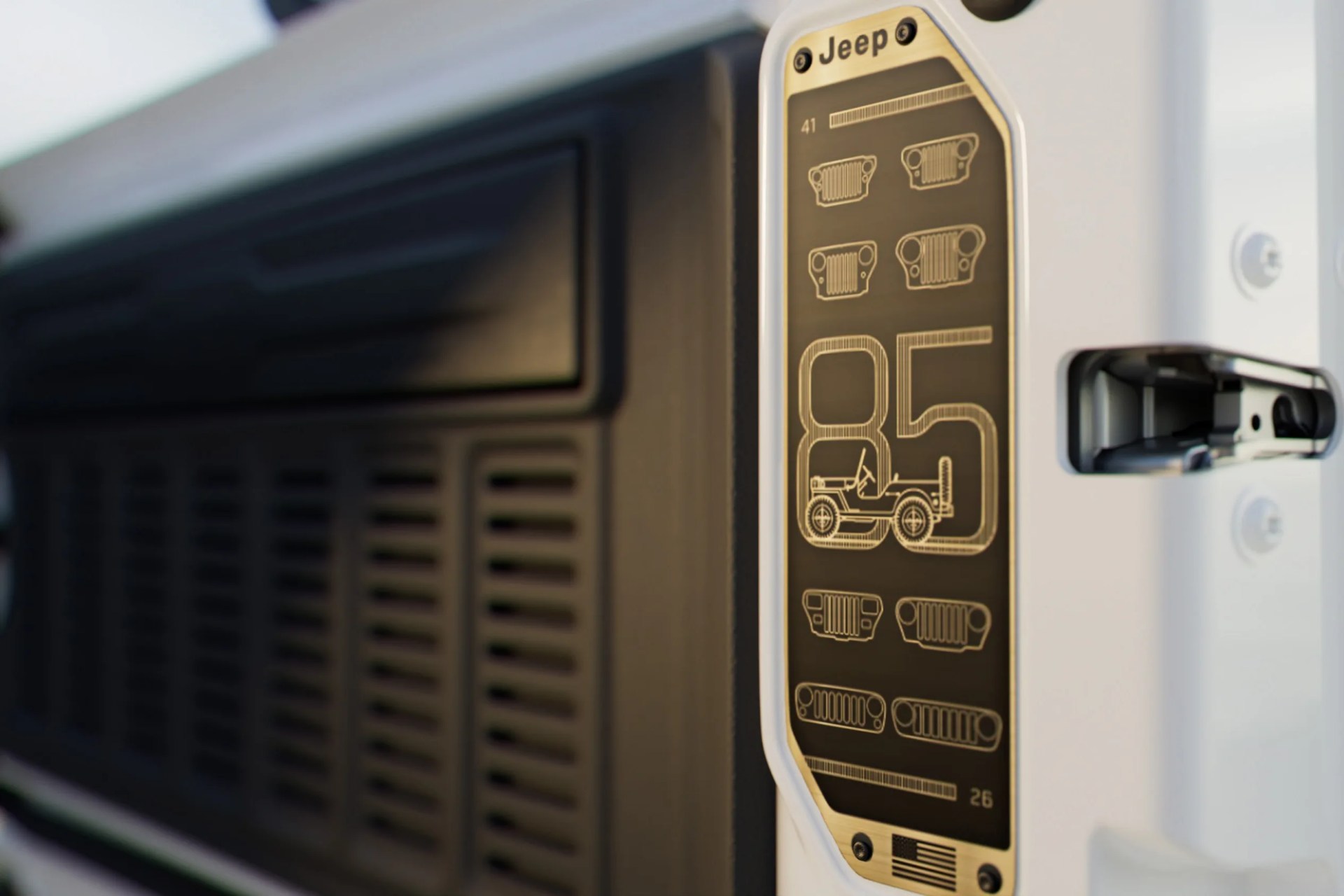 Close-up of a white Jeep door with a black and gold commemorative badge showing the number 85 and Jeep grille designs.