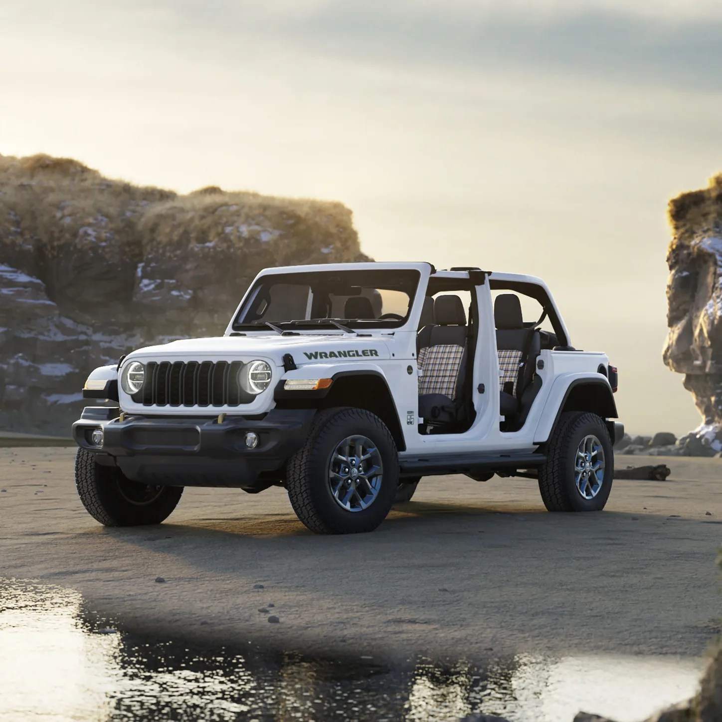 White Jeep Wrangler with open doors and plaid seat covers parked on sandy terrain near rocky cliffs.