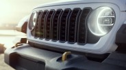 Close-up of a white vehicle front grille with round LED headlights and a black textured bumper with a gold tow hook.