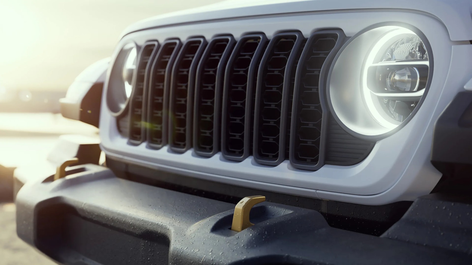 Close-up of a white vehicle front grille with round LED headlights and a black textured bumper with a gold tow hook.