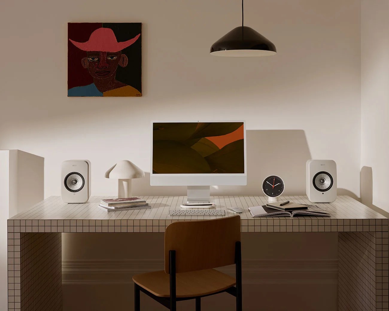 Minimalist workspace with a tiled desk, white computer, two white speakers, mushroom-shaped lamp, black clock, and wooden chair.