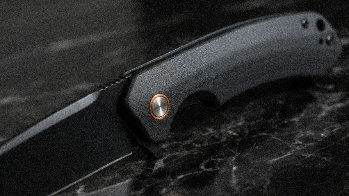 Black folding knife with textured dark gray handle and copper-accented pivot on a black marble surface.