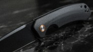 Black folding knife with textured dark gray handle and copper-accented pivot on a black marble surface.
