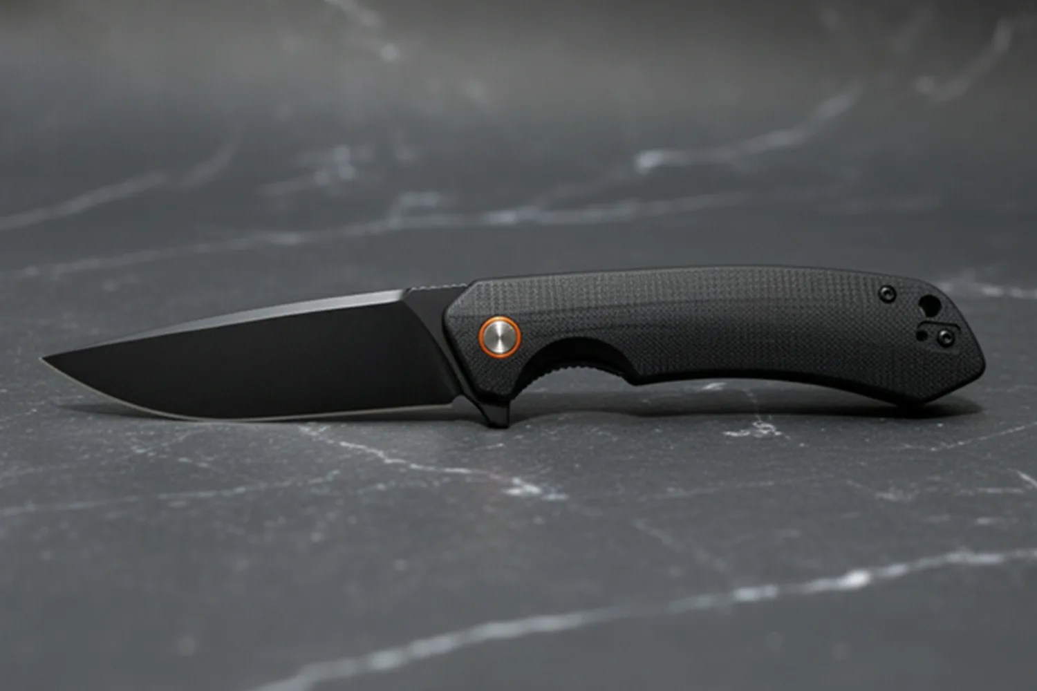 Black folding knife with textured handle and partially serrated blade on a dark marble surface.