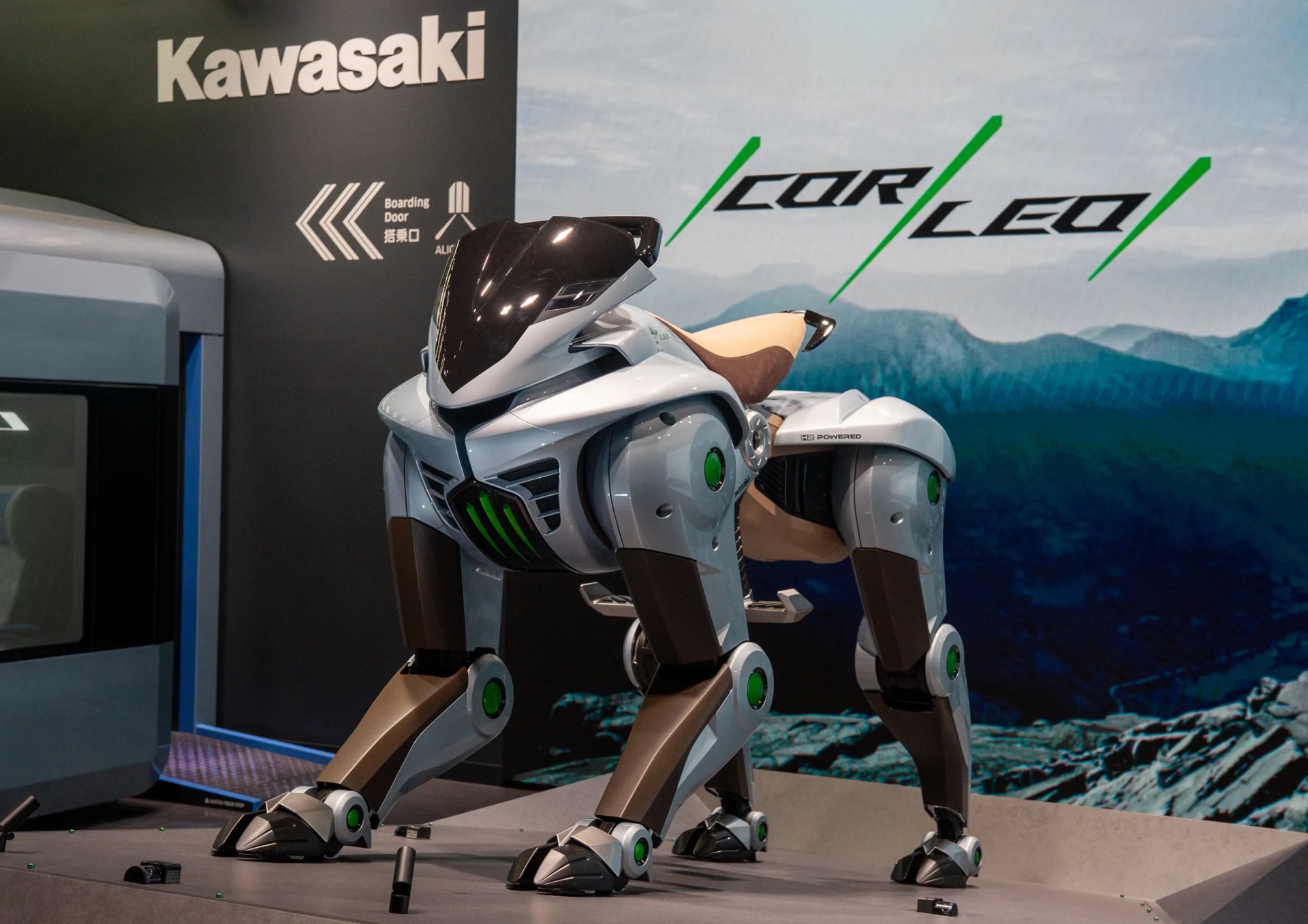 Robotic dog with a sleek white and brown body and green accents displayed at a Kawasaki booth.