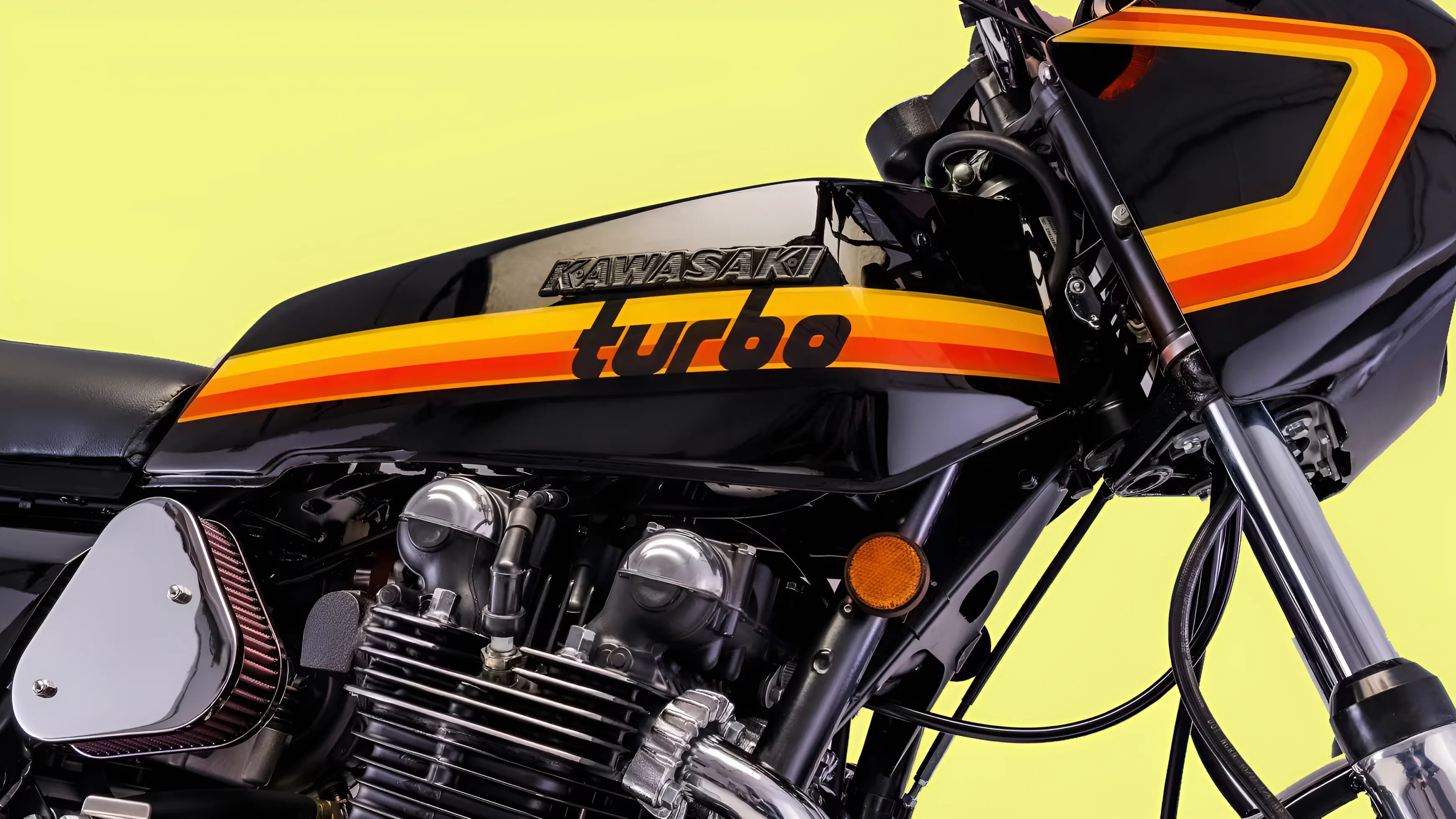Close-up of black Kawasaki Turbo motorcycle fuel tank with orange and yellow stripes and engine parts against a yellow background.