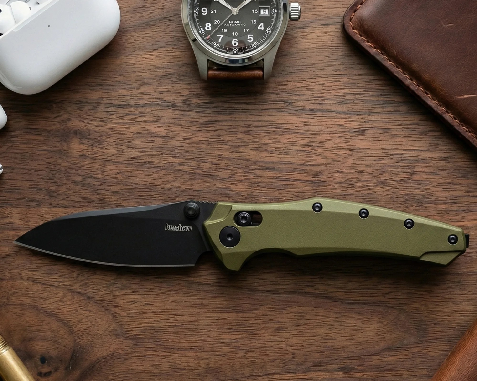 Folding knife with black blade and olive green handle on a wooden surface.