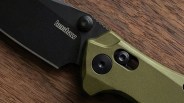 Close-up of a black Kershaw knife blade with an olive green handle on a wooden surface.