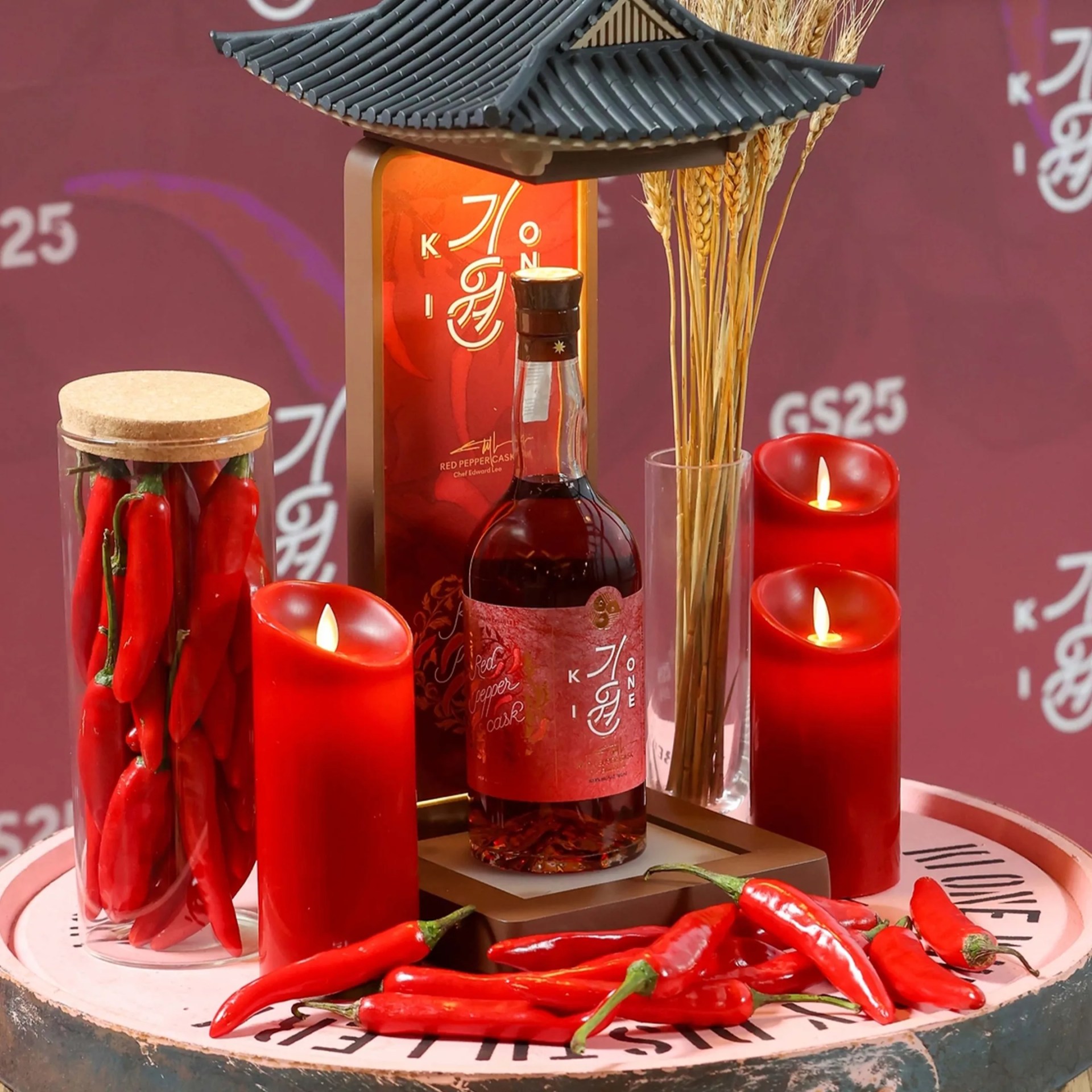 Bottle of red pepper cask liquor with red candles, fresh red chili peppers, and dried wheat stalks on a round tray.