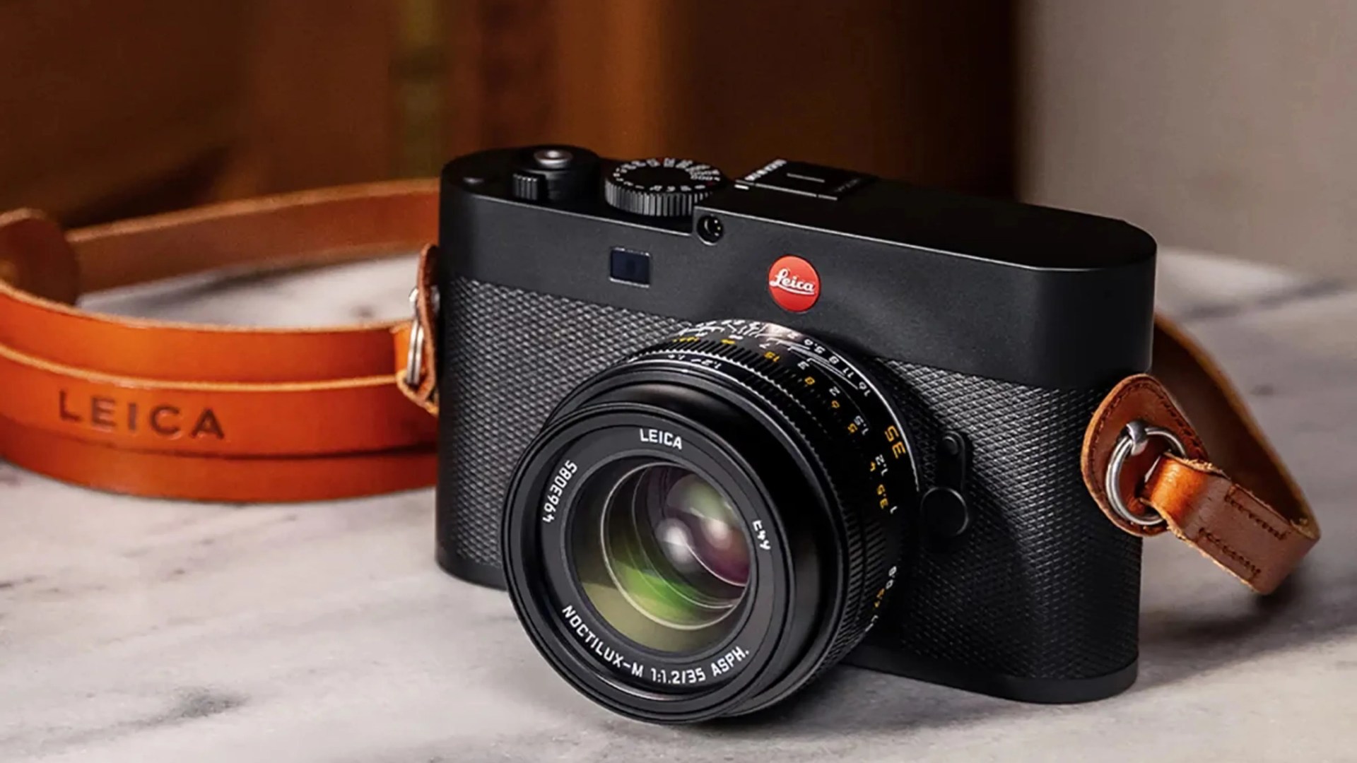 Black Leica camera with textured body and attached brown leather strap on a marble surface.
