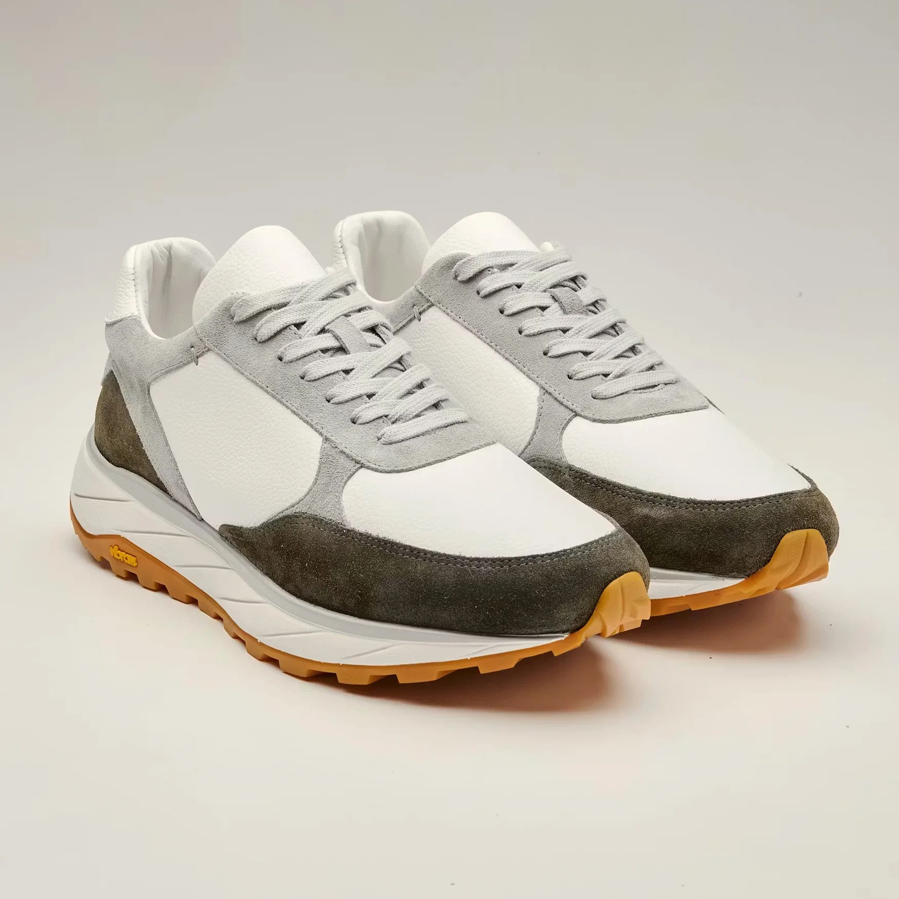 Pair of white and gray suede sneakers with gum rubber soles on a plain background.