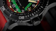 Close-up of a black watch bezel with white markings, a crown with "LUM-TEC" engraving, and a red fabric strap.