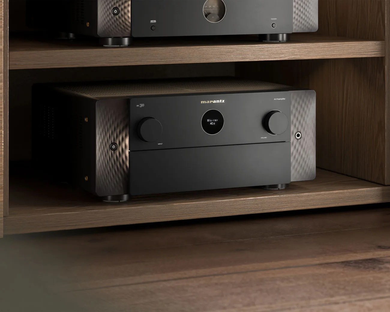 Black Marantz AV preamplifier with two large knobs and a central display on a wooden shelf.