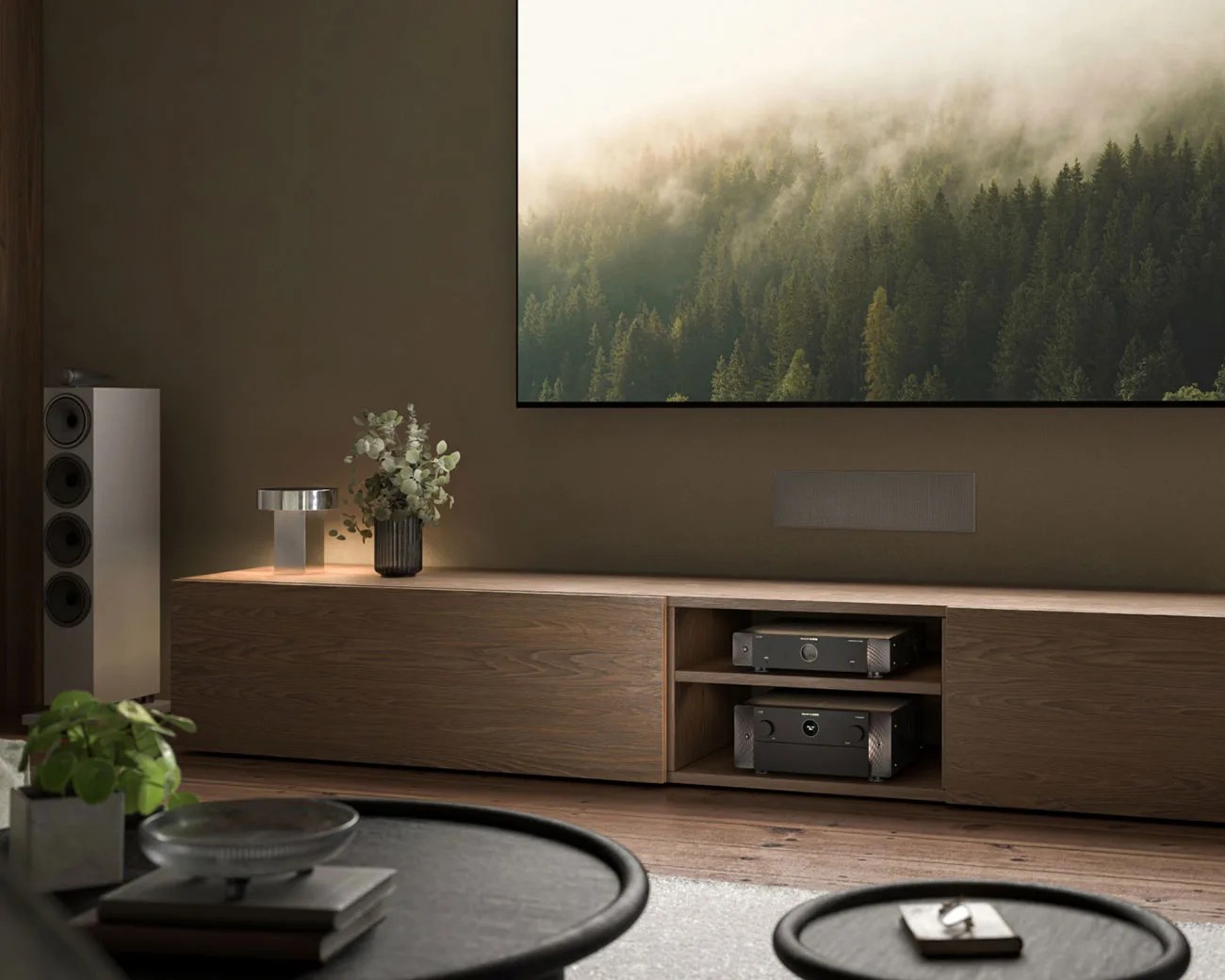 Modern living room with a wooden media console holding audio equipment, a vase with flowers, and a lamp under a large TV showing a misty forest.