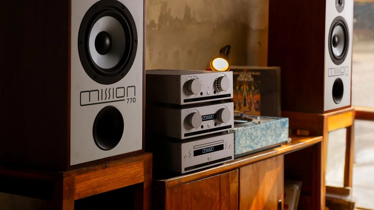 Pair of Mission 770 speakers with stacked silver audio components on a wooden cabinet.