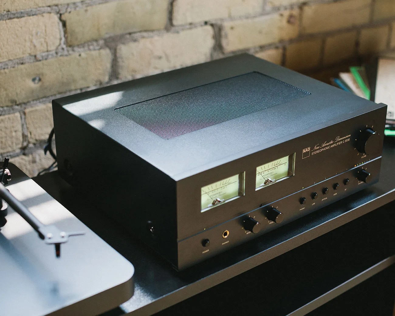 Black NAD New Acoustic Dimension stereophonic amplifier with analog meters and control knobs on a black shelf.