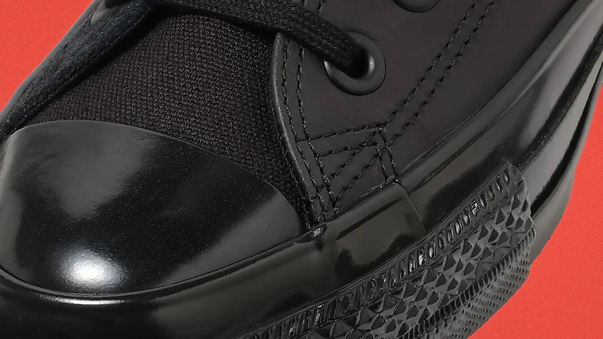 Close-up of a black sneaker toe with shiny rubber and textured fabric upper on an orange background.