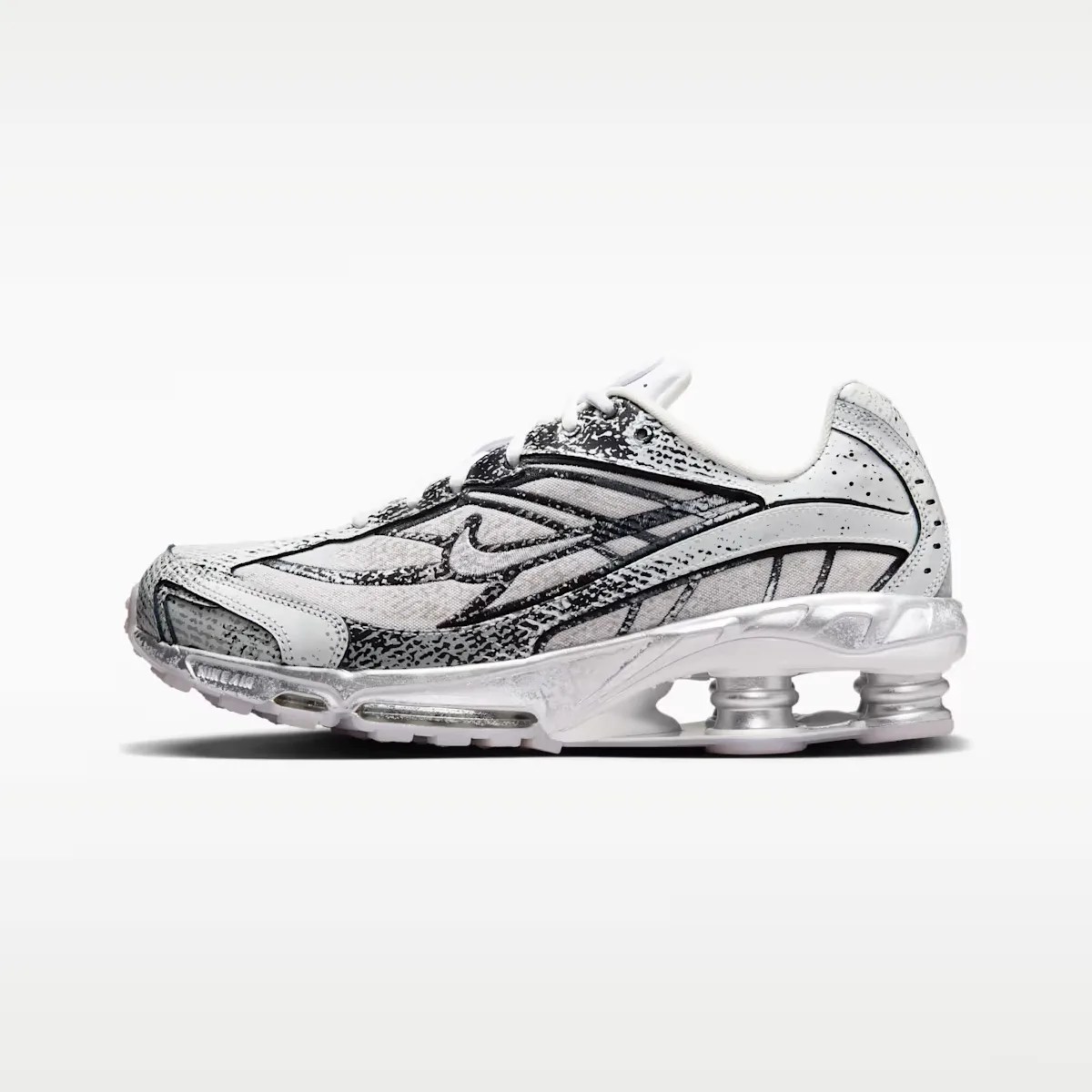 White and black Nike Shox sneaker with visible silver spring cushioning in the sole.