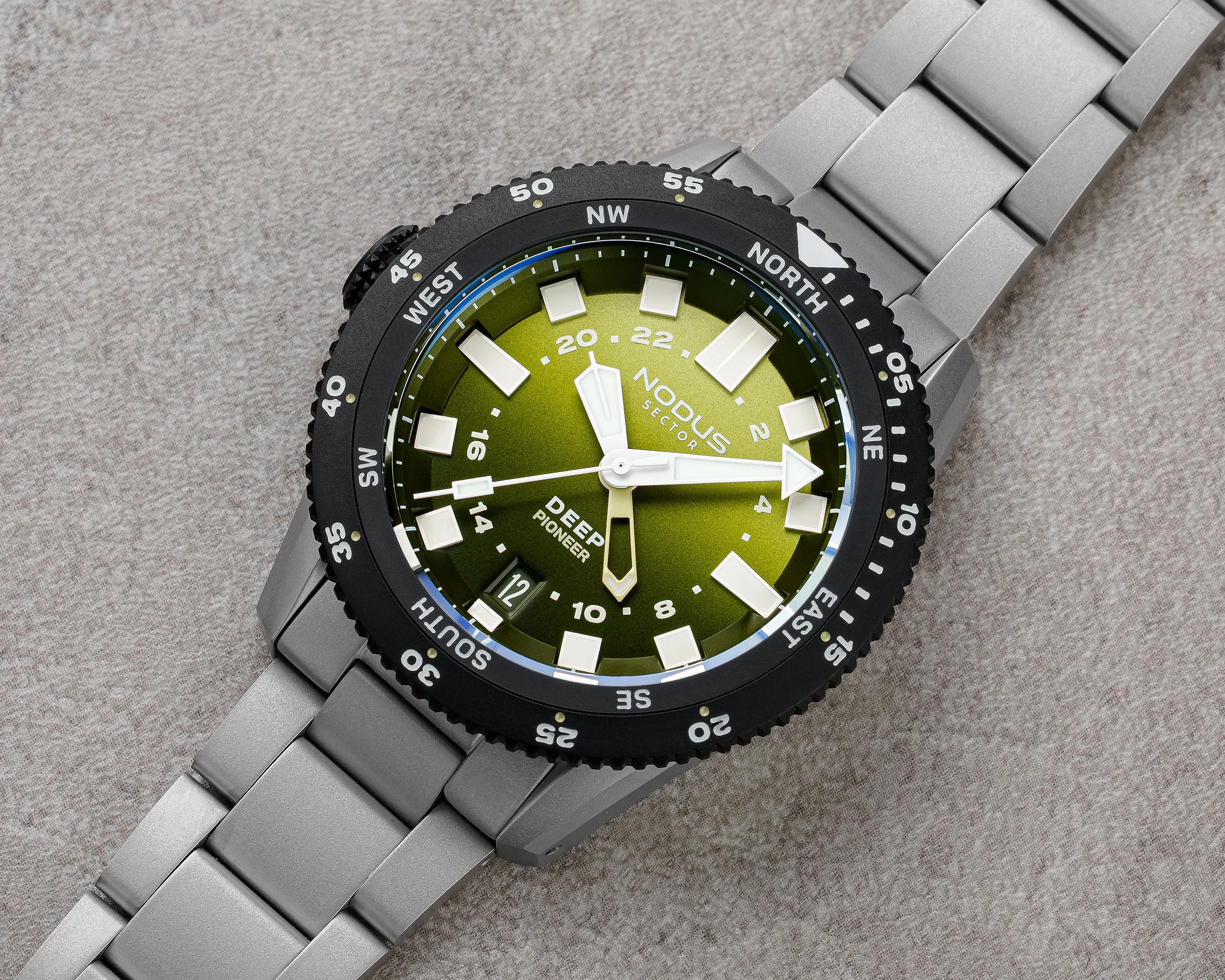 Silver metal bracelet watch with green dial, black bezel marked with compass directions, and white hour markers and hands.